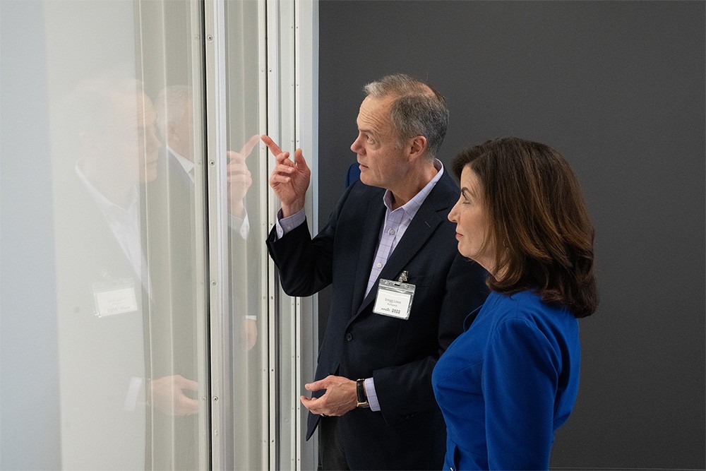 Gregg Lowe and Kathy Hochul stand together in profile, both looking through a window into the cleanroom of Wolfspeed's newest fabrication facility.